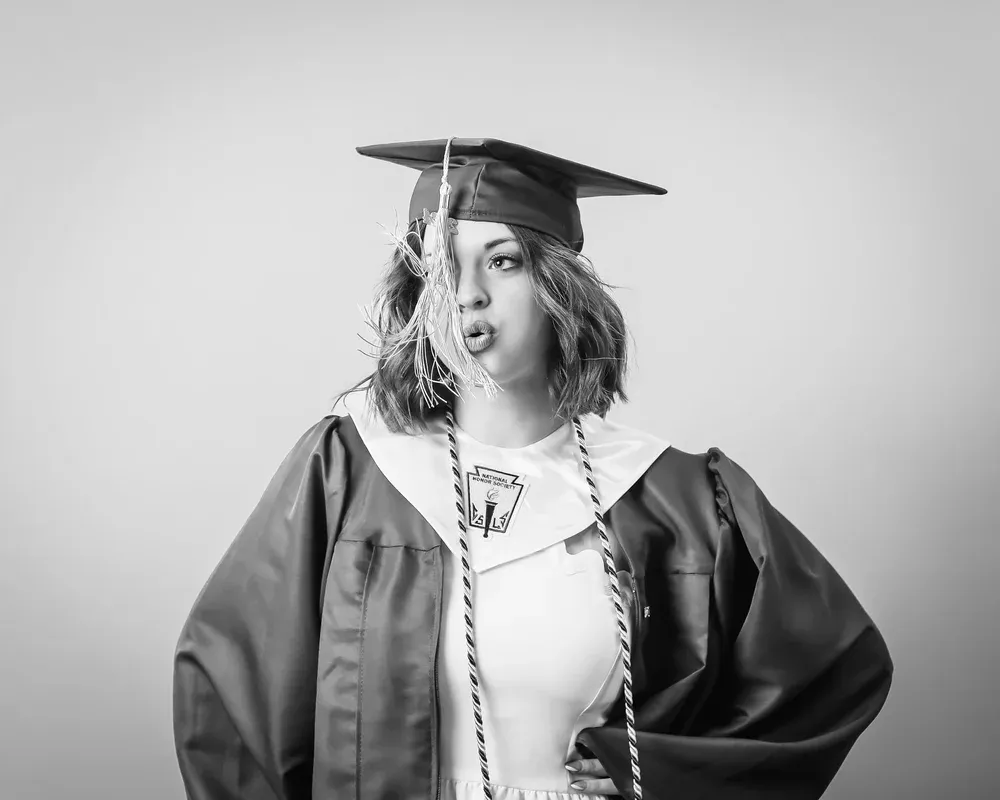 Black and white portrait of a graduate in a cap and gown making a playful duck face expression